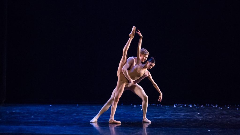 A male and female ballerina dancing in the dark on a royal blue stage.