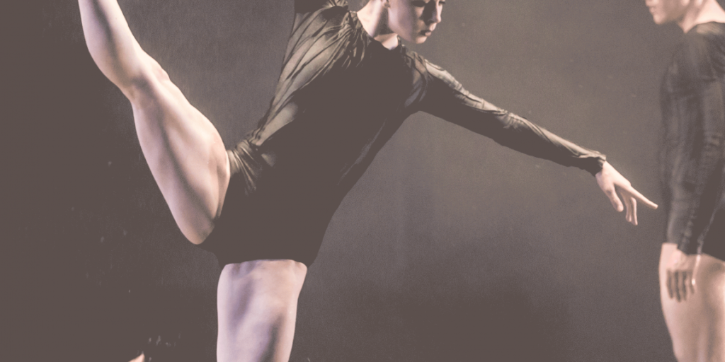 A New Vision Dance Company ballerina in a black leotard reaches out an arm with one leg stretched out and up.