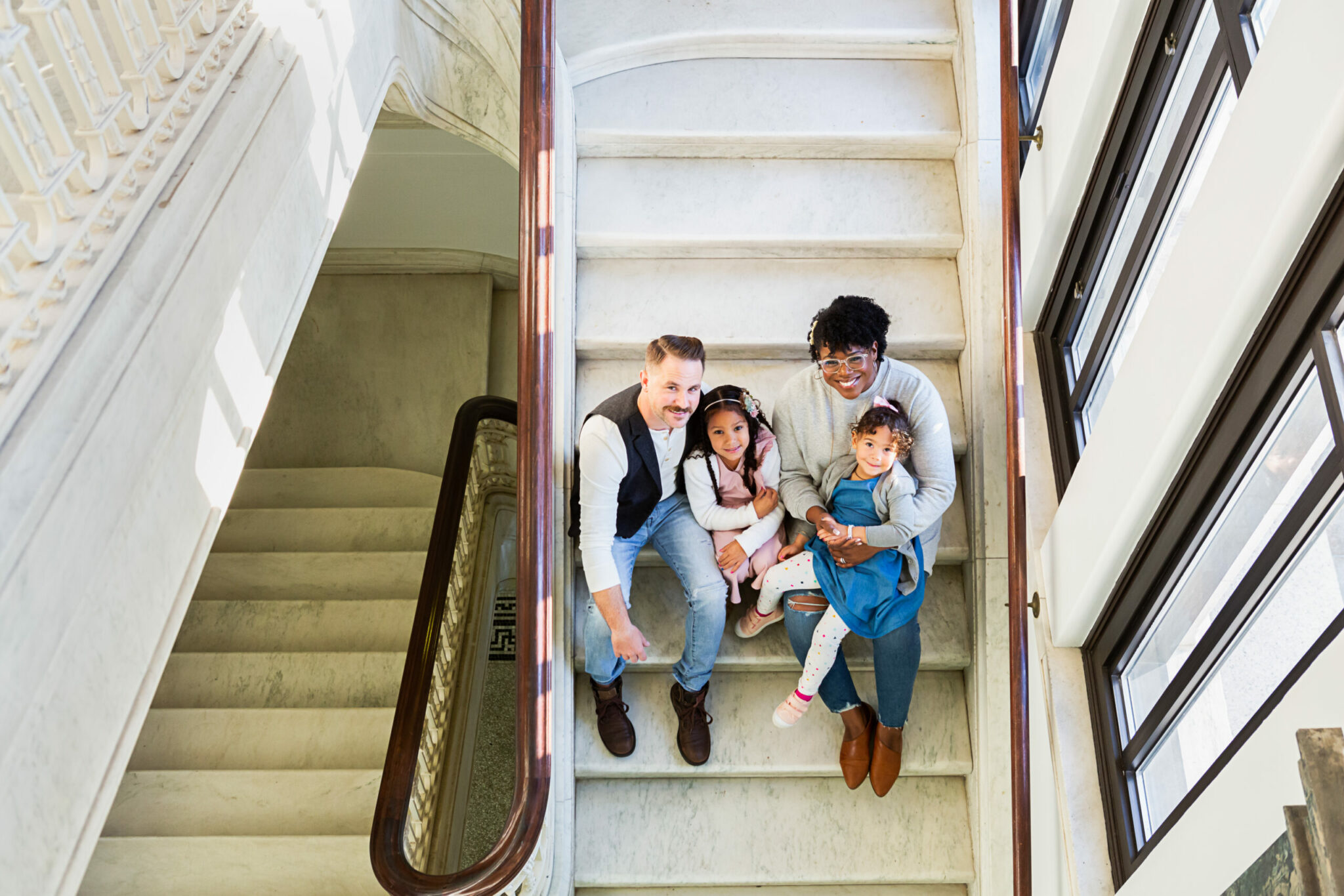 A woman and man holding two children on their lap while sitting on a staircase.