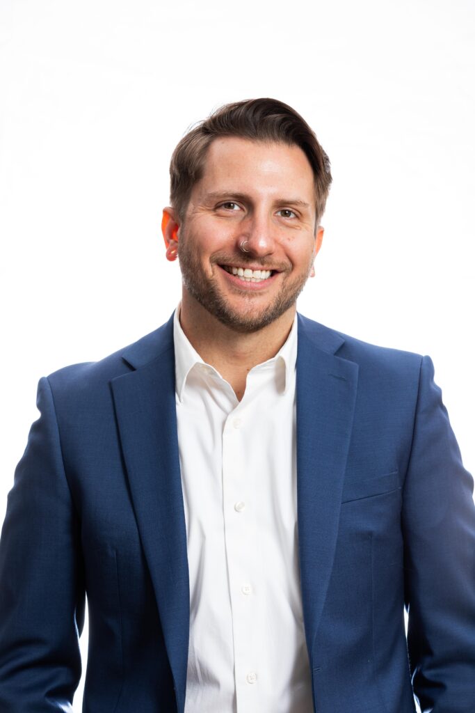 A professional realtor headshot of a smiling man with dark hair